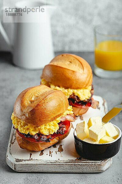 Frühstückssandwiches mit Rührei  Speck  Käse  Tomaten auf weißem Holzbrett  Glas mit frischem Orangensaft  weißer Hintergrund. Frühstück machen Konzept  selektiver Fokus