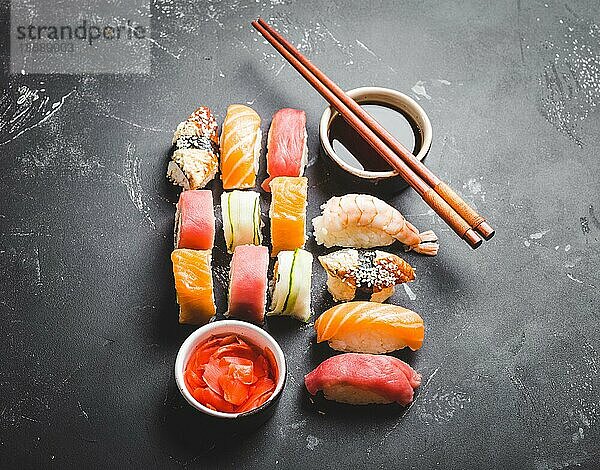 Draufsicht auf ein gemischtes japanisches Sushi-Set mit Rollen  Nigiri  Sojasauce  Ingwer  Essstäbchen auf schwarzem Betonhintergrund. Konzept für ein asiatisches Abendessen oder Mittagessen