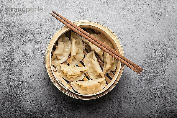 Nahaufnahme  Draufsicht auf traditionelle asiatische Teigtaschen im Bambusdämpfer mit Stäbchen auf grauem  rustikalem Steinhintergrund. Authentische chinesische Küche