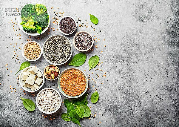 Draufsicht auf verschiedene vegane Proteinquellen mit Platz für Text: Bohnen  Linsen  Quinoa  Tofu  Gemüse  Nüsse  Kichererbsen  Reis  Hintergrund aus Stein. Gesunde  ausgewogene vegetarische Ernährung für Veganer