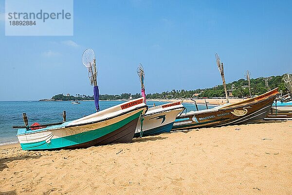 Am Strand eines der wichtigsten Touristenorte im Südwesten Sri Lankas. Auslegerboote und traditionelle Fischerboote am Strand und vor Anker