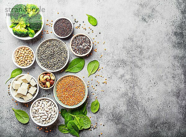 Draufsicht auf verschiedene vegane Proteinquellen mit Platz für Text: Bohnen  Linsen  Quinoa  Tofu  Gemüse  Nüsse  Kichererbsen  Reis  Hintergrund aus Stein. Gesunde  ausgewogene vegetarische Ernährung für Veganer