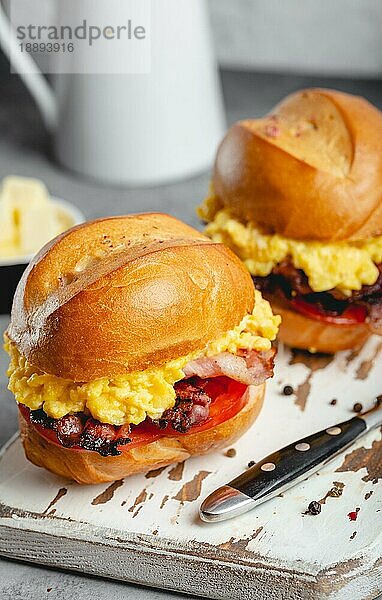 Frühstückssandwiches mit Rührei  Speck  Käse  Tomaten auf weißem Holzbrett  Glas mit frischem Orangensaft  weißer Hintergrund. Frühstück machen Konzept  selektiver Fokus