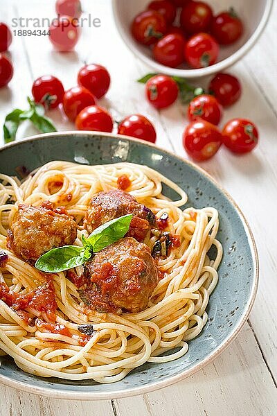 Nahaufnahme von leckeren Spaghetti mit Fleischbällchen und Tomatensauce auf einem Teller. Serviert auf einem weißen  rustikalen Holztisch. Ein italienisch-amerikanisches Gericht. Selektiver Fokus