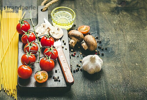 Kirschtomaten  Champignons  Spaghetti  Holzbrett  Messer. Knoblauch  Olivenöl. Kochender Hintergrund. Platz für Text. Zutaten zum Kochen. Kochendes Abendessen. Selektiver Fokus. Lebensmittel-Hintergrund