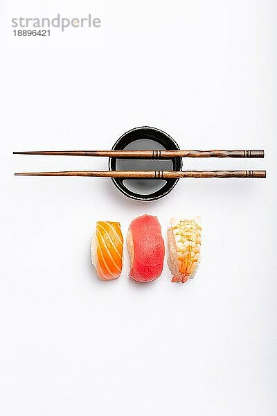 Set von verschiedenen Sushi mit Lachs  Thunfisch und Garnelen  Sojasauce und Essstäbchen auf weißem Hintergrund  Ansicht von oben. Traditionelles japanisches Sushi-Konzept  Nahaufnahme  flach gelegt