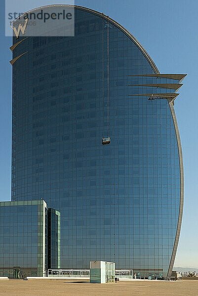 Arbeiter oder Fensterputzer auf einer Schaukelbühne im W Barcelona Hotel in Barceloneta. Das Gebäude hat eine halbmondförmige Silhouette mit 29 Stockwerken und ist ein neues Wahrzeichen Barcelonas Das riesige W Barcelona Hotel direkt am Meer im Stadtteil Barceloneta Barcelona