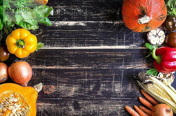 Frisches Gemüse auf einem alten  rustikalen  dunkel strukturierten Tisch. Herbst Hintergrund. Gesundes Essen Rahmen. In Scheiben geschnittener Kürbis  Paprika  Karotten  Zwiebeln  geschnittener Knoblauch  Tomaten  Rucola und Basilikum. Ansicht von oben. Platz für Text