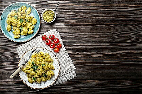 Gnocchi in Tellern mit grüner Pestosauce  Tomaten und Kräutern auf rustikalem Holzhintergrund mit Platz für Text  Nahaufnahme  Draufsicht. Traditionelles Gericht der italienischen Küche