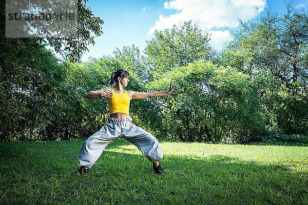 Eine Frau praktiziert Tai Chi im Freien  was zusätzliche gesundheitliche Vorteile mit sich bringt  z. B. Sonneneinstrahlung zur Vitamin D Produktion und Verbindung mit der Natur zum Stressabbau und zur Verbesserung des emotionalen Wohlbefindens