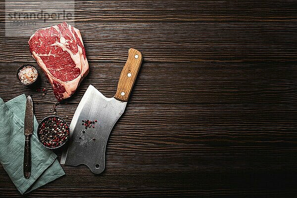 Draufsicht auf rohes frisch marmoriertes Fleisch Steak Ribeye  rustikales Fleischbeil  Gewürze auf hölzernem Hintergrund mit Platz für Text. Kochen saftig Bio-Steak Metzgerei Konzept  gesunde saubere Ernährung  Nahaufnahme