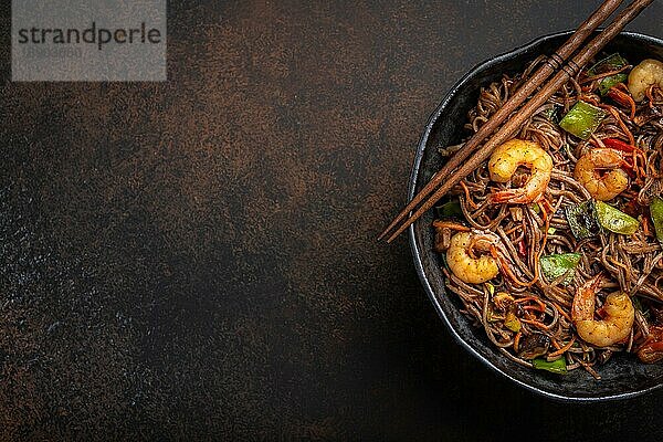 Nahaufnahme von chinesischen Soba-Rührbratnudeln mit Garnelen und Gemüse in einer rustikalen Keramikschüssel auf einem Betonhintergrund  Nahaufnahme  Draufsicht. Traditionelles asiatisches/thailändisches Gericht  Platz für Text