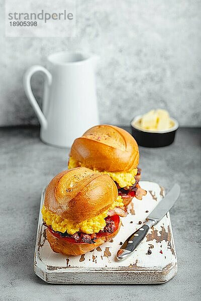 Frühstückssandwiches mit Rührei  Speck  Käse  Tomaten auf weißem Holzbrett  Glas mit frischem Orangensaft  weißer Hintergrund. Frühstück machen Konzept  selektiver Fokus