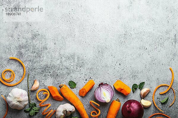 Lebensmittel Hintergrund mit freiem Raum für Text. Nahaufnahme  Draufsicht auf geschnittene frische rohe Karotte  Zwiebeln  Knoblauch  Kräuter auf rustikalem grauen Stein Hintergrund  Kochen  vegetarisches Essen oder gesunde Ernährung Konzept