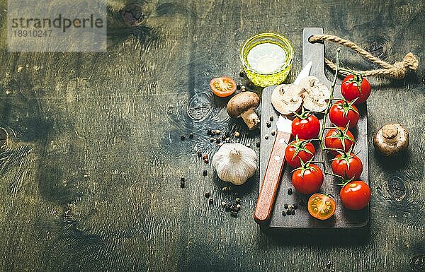 Kirschtomaten  Champignons auf Holzbrett  Messer. Mit Knoblauch  Olivenöl. Kochender Hintergrund. Platz für Text. Rohe Zutaten zum Kochen. Essen kochen. Selektiver Fokus. Lebensmittel-Hintergrund