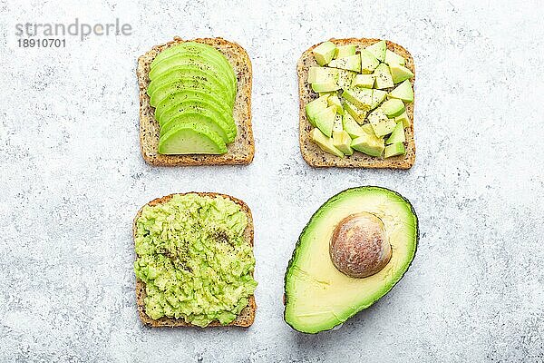 Verschiedene Arten von Avocado-Toasts und eine Hälfte der ganzen Avocado über weißen Stein Hintergrund  Konzept. Wege der Herstellung und Servieren leckeres gesundes Frühstück Avocado-Sandwich  Draufsicht  Nahaufnahme