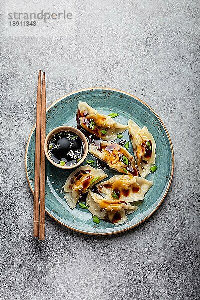 Nahaufnahme  Draufsicht auf traditionelle asiatische Teigtaschen in blauem Teller mit Sojasauce und Essstäbchen auf grauem  rustikalem Steinhintergrund. Authentische chinesische Küche