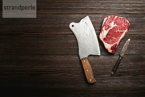 Draufsicht auf rohes  frisch marmoriertes Fleisch Steak Ribeye mit rustikalem Fleischbeil auf hölzernem Hintergrund mit Platz für Text. Kochen saftige Bio-Steak oder Metzgerei Konzept  gesunde saubere Ernährung  Nahaufnahme