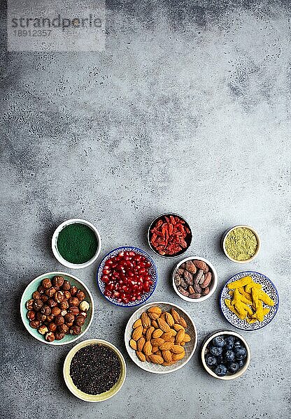 Set von verschiedenen Superfoods in Schalen auf steingrauem Hintergrund: Spirulina  Goji-Beere  Kakao  Matcha-Grüntee  Quinoa  Chia-Samen  Blaubeeren  Nüsse für ein glückliches  gesundes Leben  Draufsicht  Kopierraum