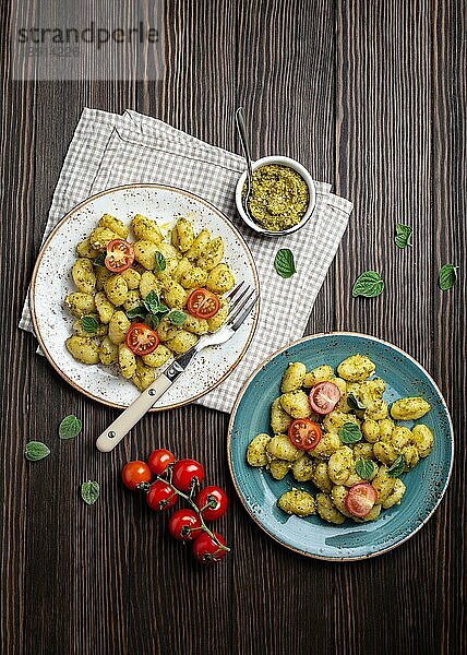 Gnocchi in Tellern mit grüner Pestosauce  Tomaten und Kräutern auf rustikalem Holzhintergrund  Nahaufnahme  Draufsicht. Traditionelles Gericht der italienischen Küche