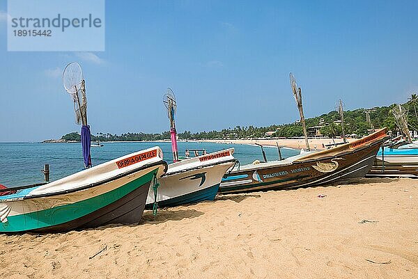 Unawatuna. Am Strand eines der wichtigsten Touristenzentren im Südwesten Sri Lankas. Touristen nehmen ein Sonnenbad und treiben Wassersport. Auslegerboote und traditionelle Fischerboote am Strand