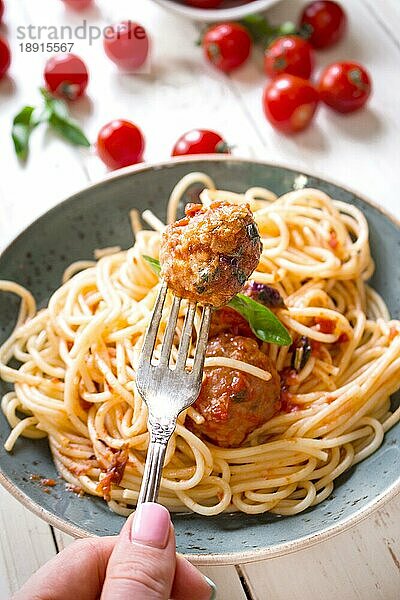 Nahaufnahme einer leckeren Frikadelle auf einer Gabel. Spaghetti mit Fleischbällchen und Tomatensauce auf einem Teller. Serviert auf einem weißen  rustikalen Holztisch. Ein italienisch-amerikanisches Gericht. Selektiver Fokus