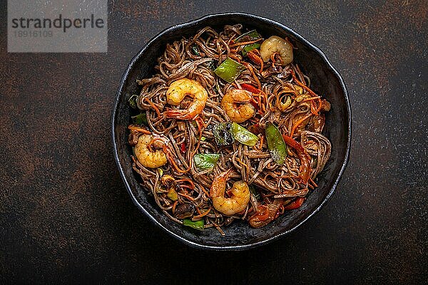 Nahaufnahme von chinesischen Soba-Rührnudeln mit Garnelen und Gemüse in einer rustikalen Keramikschüssel auf einem Betonhintergrund  Nahaufnahme  Draufsicht. Traditionelles asiatisches/thailändisches Gericht  Mahlzeit im chinesischen Stil