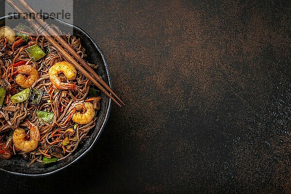 Nahaufnahme von chinesischen Soba-Rührbratnudeln mit Garnelen und Gemüse in einer rustikalen Keramikschüssel auf einem Betonhintergrund  Nahaufnahme  Draufsicht. Traditionelles asiatisches/thailändisches Gericht  Platz für Text