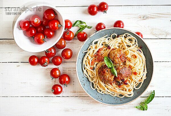 Nahaufnahme von leckeren Spaghetti mit Fleischbällchen und Tomatensauce auf einem Teller. Serviert auf einem weißen  rustikalen Holztisch. Ein italienisch-amerikanisches Gericht. Ansicht von oben. Selektiver Fokus