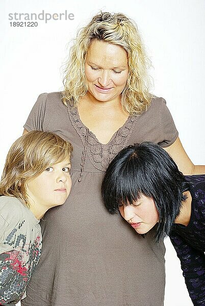 Sohn und Tochter legen Kopf auf Bauch der schwangeren Mutter
