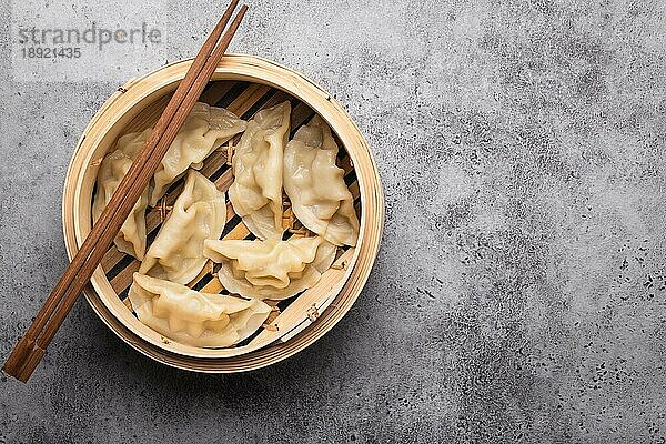 Nahaufnahme  Draufsicht auf traditionelle asiatische Teigtaschen im Bambusdämpfer mit Stäbchen auf grauem  rustikalem Steinhintergrund mit Platz für Text. Authentische chinesische Küche  Platz zum Kopieren