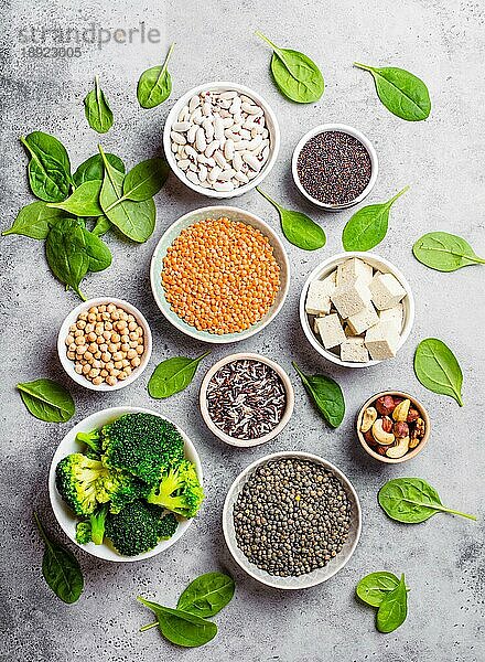 Draufsicht auf verschiedene vegane Proteinquellen: Bohnen  Linsen  Quinoa  Tofu  Gemüse  Spinat  Nüsse  Kichererbsen  Reis  rustikaler Hintergrund aus Stein. Gesunde  ausgewogene vegetarische Ernährung für Veganer