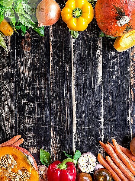 Frisches Gemüse auf einem alten  rustikalen  dunkel strukturierten Tisch. Herbst Hintergrund. Gesundes Essen Rahmen. In Scheiben geschnittener Kürbis  Paprika  Karotten  Zwiebeln  geschnittener Knoblauch  Tomaten  Rucola und Basilikum. Ansicht von oben. Platz für Text