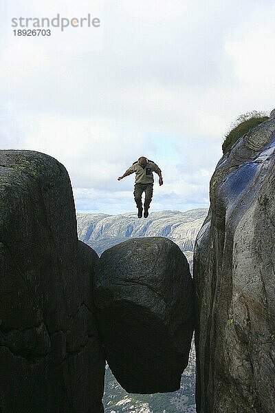 Ein Tourist hüpft 1000m über dem Lysefjord auf dem Kjeragbolzen herum (keine Fotomontage)  Norwegen  Europa