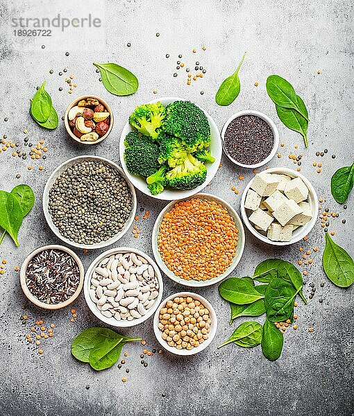 Draufsicht auf verschiedene vegane Proteinquellen: Bohnen  Linsen  Quinoa  Tofu  Gemüse  Spinat  Nüsse  Kichererbsen  Reis  rustikaler Hintergrund aus Stein. Gesunde ausgewogene vegetarische Ernährung für Veganer