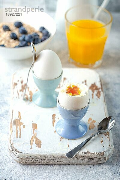 Frische weich gekochte Eier  Haferflocken mit Blaubeeren  Kaffee  Orangensaft  Milch. Weißer Beton rustikalen Hintergrund. Weiche Eier  gesundes Frühstück. Selektiver Fokus. Leckeres leichtes Fitness-Frühstück. Nahaufnahme