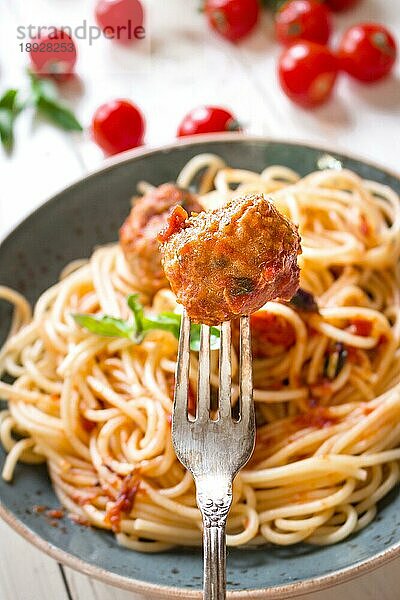 Nahaufnahme einer leckeren Frikadelle auf einer Gabel. Spaghetti mit Fleischbällchen und Tomatensauce auf einem Teller. Serviert auf einem weißen  rustikalen Holztisch. Ein italienisch-amerikanisches Gericht. Selektiver Fokus