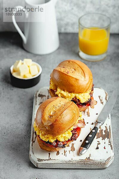 Frühstückssandwiches mit Rührei  Speck  Käse  Tomaten auf weißem Holzbrett  Glas mit frischem Orangensaft  weißer Hintergrund. Frühstück machen Konzept  selektiver Fokus