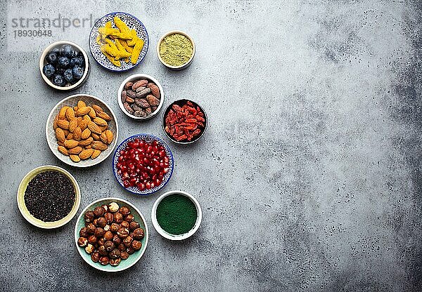 Set von verschiedenen Superfoods in Schalen auf steingrauem Hintergrund: Spirulina  Goji-Beere  Kakao  Matcha-Grüntee  Quinoa  Chia-Samen  Blaubeeren  Nüsse für ein glückliches  gesundes Leben  Draufsicht  Kopierraum
