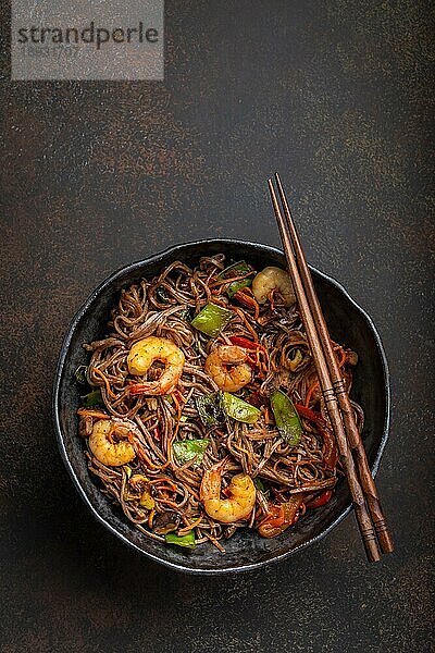 Nahaufnahme von chinesischen Soba-Rührnudeln mit Garnelen und Gemüse in einer rustikalen Keramikschüssel auf einem Betonhintergrund  Nahaufnahme  Draufsicht. Traditionelles asiatisches/thailändisches Gericht  Mahlzeit im chinesischen Stil