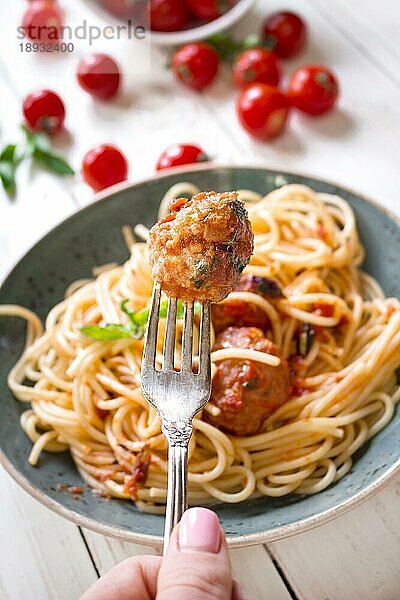 Nahaufnahme einer leckeren Frikadelle auf einer Gabel. Spaghetti mit Fleischbällchen und Tomatensauce auf einem Teller. Serviert auf einem weißen  rustikalen Holztisch. Ein italienisch-amerikanisches Gericht. Selektiver Fokus