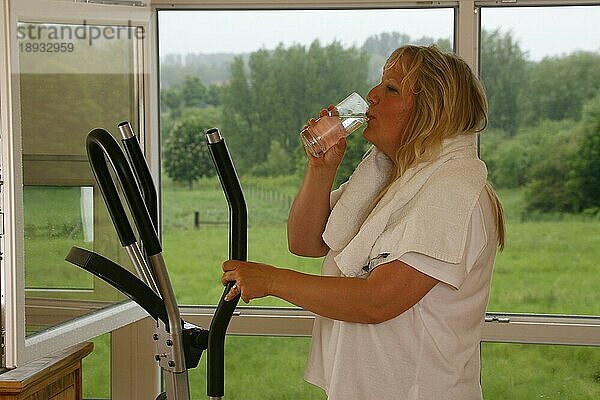 Frau auf Crosstrainer  trinkt Wasser
