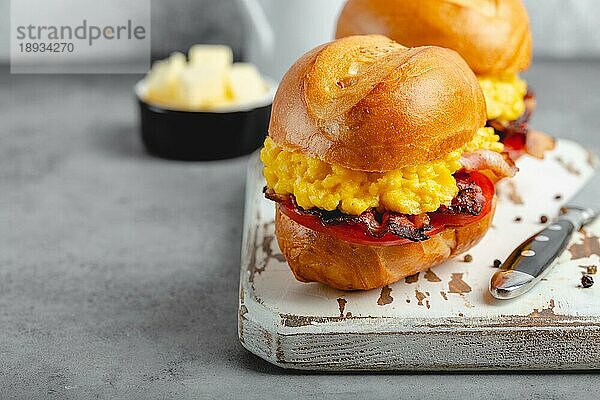 Frühstückssandwiches mit Rührei  Speck  Käse  Tomaten auf weißem Holzbrett  Glas mit frischem Orangensaft  weißer Hintergrund. Frühstück machen Konzept  selektiver Fokus