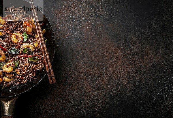 Nahaufnahme von chinesischen Soba-Rührnudeln mit Garnelen und Gemüse in einer alten  rustikalen Wokpfanne auf einem Betonhintergrund  Nahaufnahme  Draufsicht. Traditionelles asiatisches/thailändisches Gericht  Platz für Text