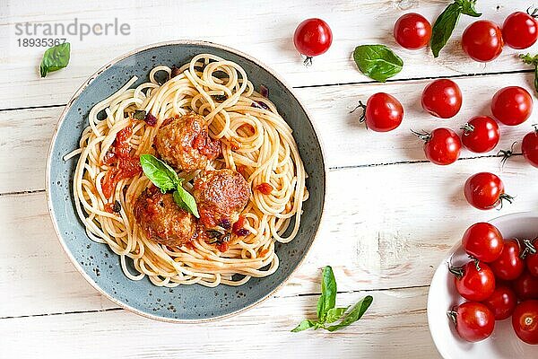 Nahaufnahme von leckeren Spaghetti mit Fleischbällchen und Tomatensauce auf einem Teller. Serviert auf einem weißen  rustikalen Holztisch. Ein italienisch-amerikanisches Gericht. Ansicht von oben. Selektiver Fokus