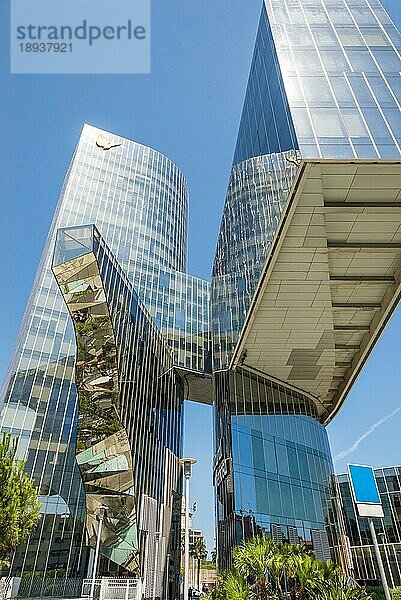 Der Torre Mare Nostrum als modernes Hochhaus in Froschperspektive im Stadtteil Barceloneta von Barcelona. Die Spiegel am Wolkenkratzer spielen mit Licht  Menschen und Dingen in der Umgebung. Das außergewöhnliche Hochhaus ist Hauptsitz eines großen Gasunternehmens