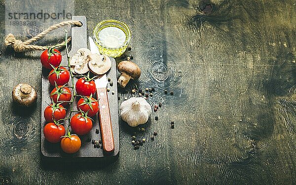 Kirschtomaten  Champignons auf Holzbrett  Messer. Mit Knoblauch  Olivenöl. Kochender Hintergrund. Platz für Text. Rohe Zutaten zum Kochen. Essen kochen. Selektiver Fokus. Lebensmittel Hintergrund