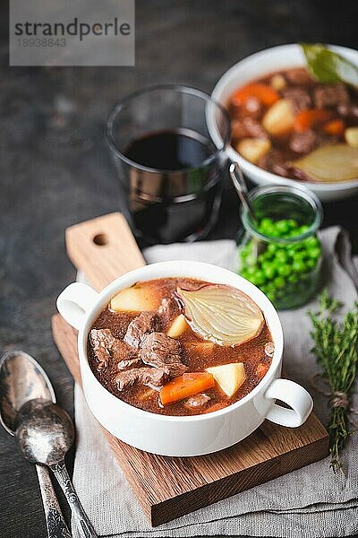 Fleischeintopf mit Rindfleisch  Kartoffeln  Karotten  Zwiebeln  Gewürze  grüne Erbsen. Langsam gekochter Fleischeintopf  Schüssel  hölzerner Hintergrund. Heißes Herbst-/Wintergericht. Selektiver Fokus. Wohlfühlessen. Hausgemachte Suppe/Ragout/Kasserolle