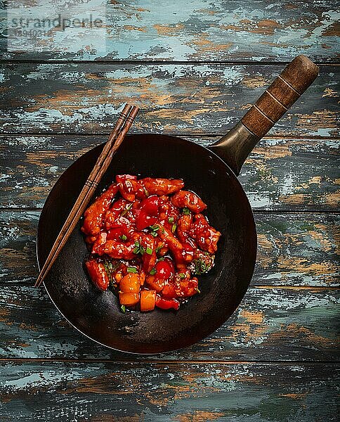 Asiatischen oder chinesischen Stil leckeres Huhn in süß-saurer Soße in schwarzem rustikalen Wok-Pfanne auf bunten hölzernen Hintergrund serviert. Asiatisches Abendessen Konzept  Draufsicht  Nahaufnahme