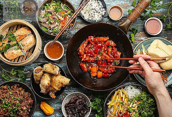 Verschiedene chinesische Gerichte auf einem Tisch mit einer männlichen Hand  die Stäbchen von oben hält. Voller und festlicher Tisch mit allen traditionellen chinesischen Gerichten  Abendessen oder Buffet im asiatischen Stil  Ansicht von oben